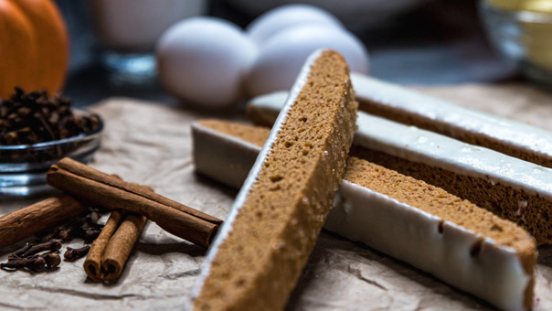 Iced biscotti slices with cinnamon sticks, cloves, and eggs on a rustic surface, warm brown and cream tones with an autumnal feel